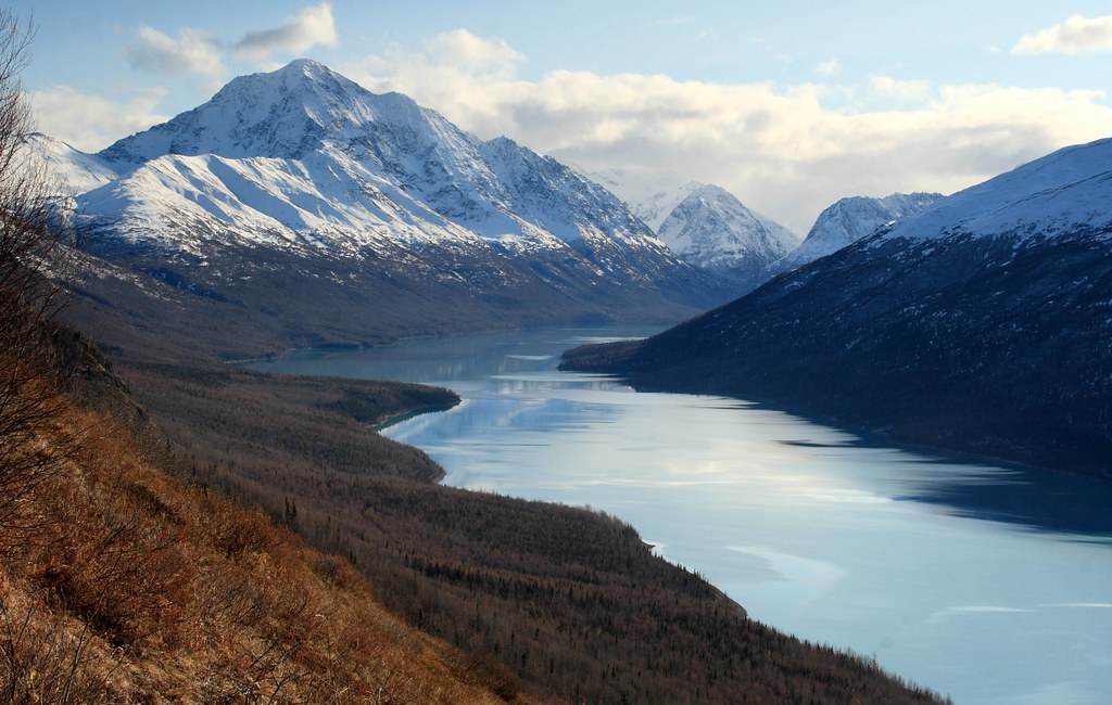 A breathtaking view of Eklutna Lake from the Twin Peaks Trail near Anchorage, Alaska, surrounded by rugged mountains and lush greenery.